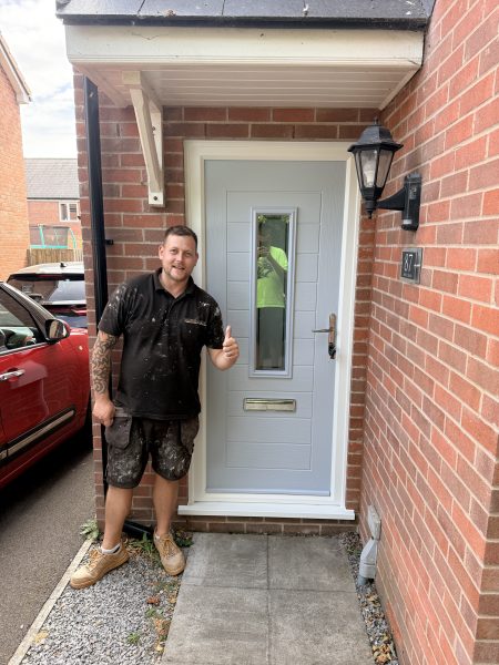 Kyle from Goldhill Glazing beside a new grey composite door in Shaftesbury